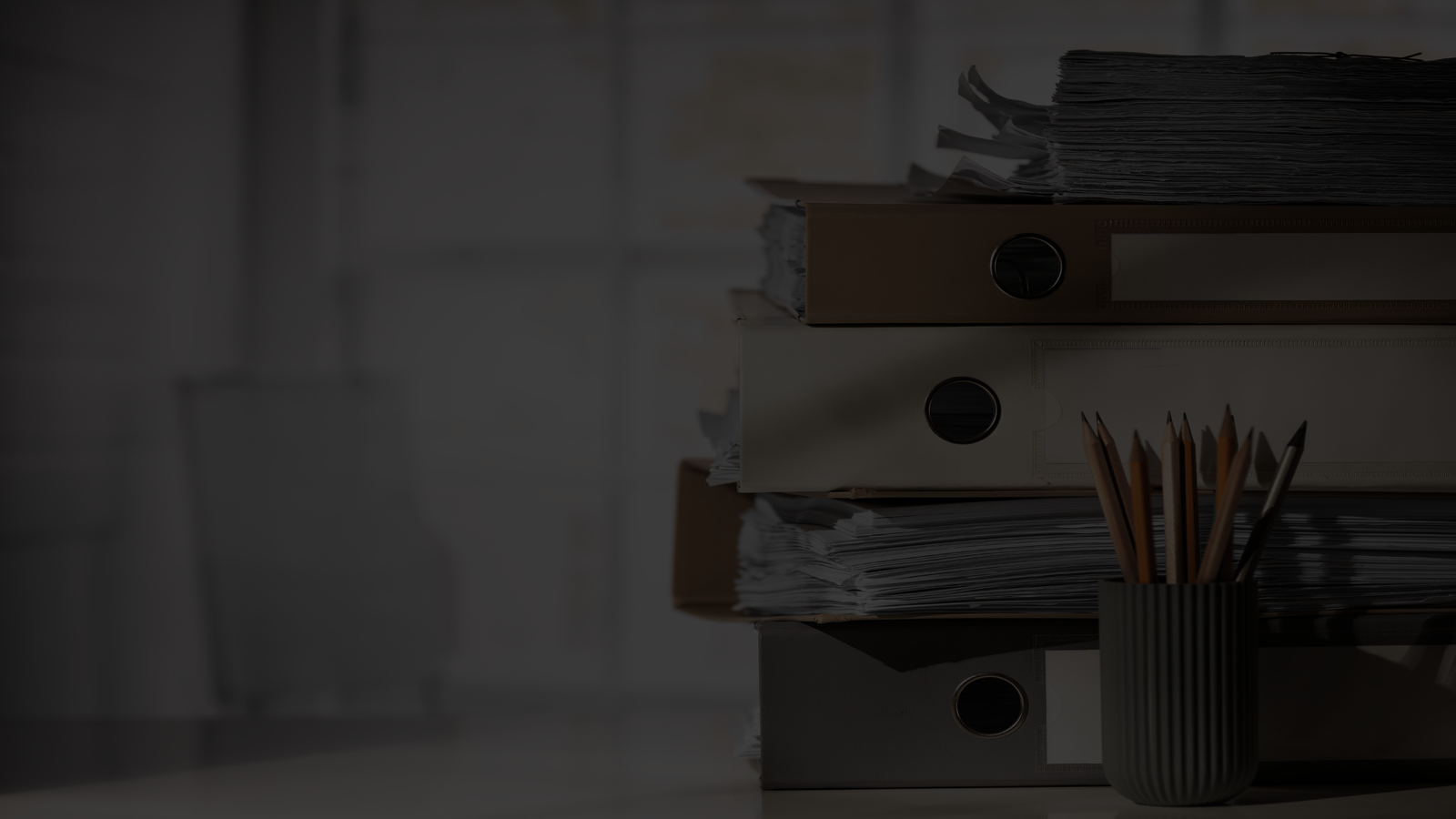 Photo d'une pile de classeurs remplis de feuilles et un pot contenant une dizaine de crayons en bois.